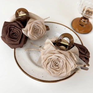 Detail of elegant fabric rose hair claw clips in coffee and beige on a white ceramic plate