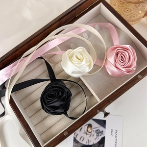 Elegant satin rose flower chokers in black, white, and pink on a vintage wooden tray