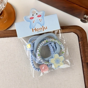 Detail of blue hair scrunchie set with flower and duck charms in clear packaging