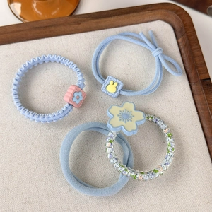 Close-up of light blue floral scrunchies and beaded elastic hair ties on linen