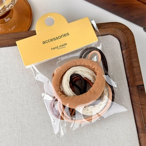 Dettaglio di elastici per capelli color terra beige e marrone con confezione in cartone