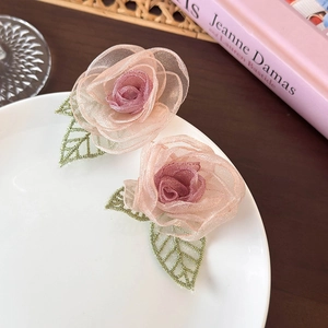 Détail de boucles d'oreilles roses en résille avec feuilles brodées vertes sur une assiette blanche