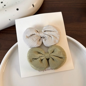 Détail de pinces à cheveux à nœuds en beige et vert olive sur une carte de présentation