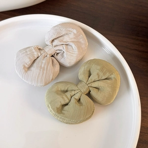 Détail des barrettes nœuds papillon en tissu texturé crème et vert sauge sur une assiette