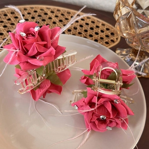 Pink rose flower hair claw clips set with white feathers and crystals on a ceramic tray
