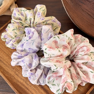Three floral chiffon scrunchies in purple and yellow on a rustic wooden tray for women