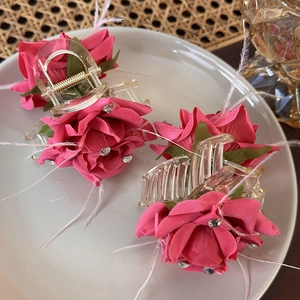 Pink fabric rose hair claws with feathers and sequins on a minimalist white tray