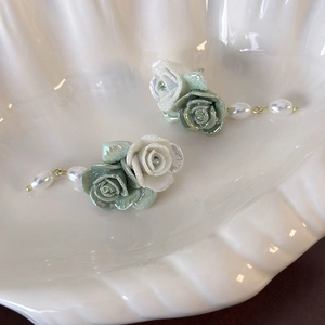 Close-up of vintage ceramic green rose earrings with white pearls in a shell tray