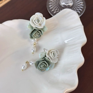 Detail of vintage ceramic rose earrings with pearls on a textured white tray