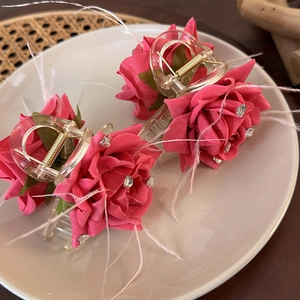 Detailed close-up of two pink rose hair clips with feathers and rhinestones in a tray