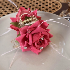 Detail of pink fabric rose hair claw clip with heart rhinestones and white feathers
