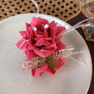 Close-up of pink fabric rose hair claw clip with delicate white feathers and sparkling rhinestones