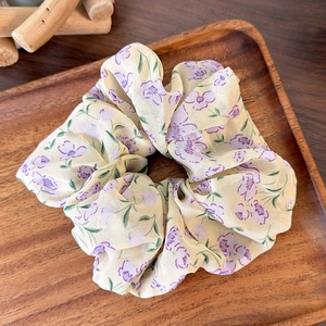 Detail of floral chiffon hair scrunchie with purple flowers on a wooden tray