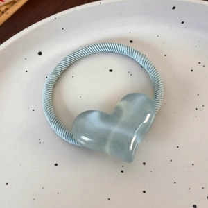 Détail d'un élastique à cheveux bleu clair avec pendentif cœur à effet œil de chat