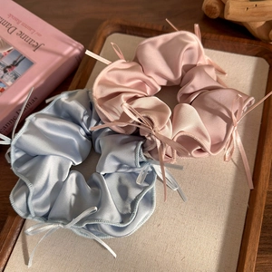 Dettaglio di scrunchie in raso rosa e blu con piccoli fiocchi di nastro in vassoio