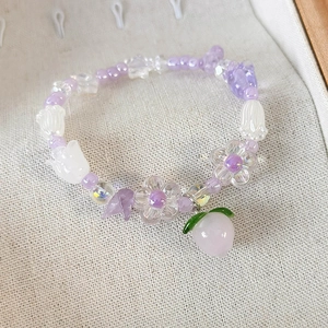 Détail macro d'un bracelet de perles fait main avec fleurs violettes et pendentif pêche