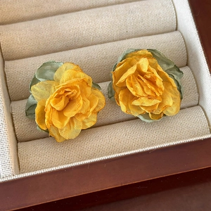 Macro shot of yellow fabric flower earrings with green leaves in a beige jewelry box