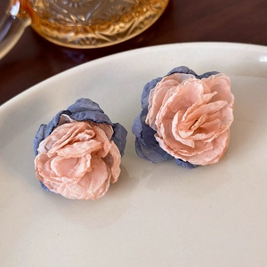 Macro detail of multilayered fabric mesh flower earrings in soft pink and blue