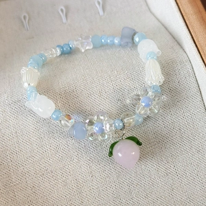 Détail d'un bracelet en perles avec pendentif pêche, fleurs bleues et perles blanches