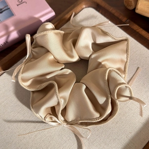 Dettaglio dell'elastico in raso champagne con fiocchetti su un vassoio di legno