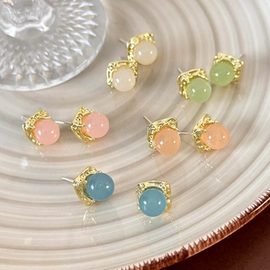 Close-up of geometric resin stud earrings in pastel colors on a textured ceramic plate