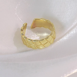 Macro shot of minimalist gold braided ring with textured weave pattern on white silk fabric