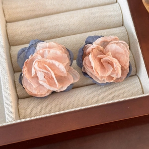 Detailed macro view of peach and blue layered fabric flower earrings on white linen