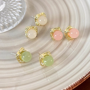Detail of square gold textured base with pink, green and white bead earrings on a ceramic plate