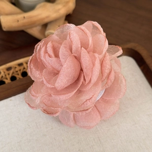 Détail de la pince à cheveux avec grande fleur en tulle rose superposée sur plateau bois