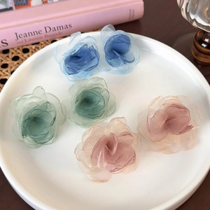 Detail of multi-layered mesh fabric flower earrings in blue, green and pink on a white plate