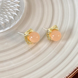 Detail of pink cabochon earrings with hammered gold metal edges on a ceramic plate