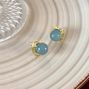Detailed view of square gold stud earring with a translucent blue bead on a ceramic tray