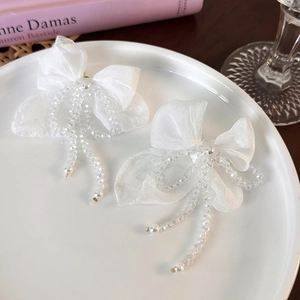 Detail of white chiffon bow earrings with long beaded tassels and pearls on ceramic plate