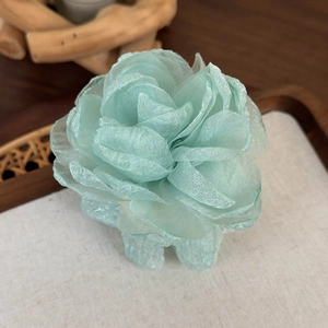 Détail d'une pince à cheveux fleur en mousseline vert menthe sur un plateau en bois