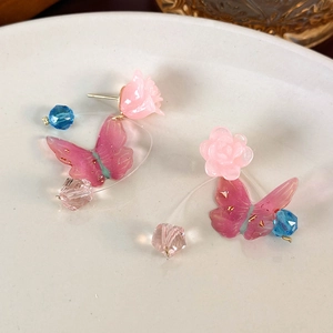 Pink floral and butterfly crystal drop earrings on a white ceramic display tray