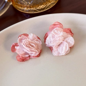 Close-up of pink layered mesh flower earrings on a white ceramic plate with a glass accent