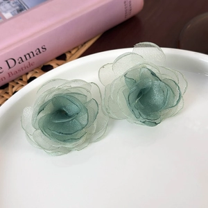 Detail view of light green mesh fabric rose earrings resting on a white ceramic plate