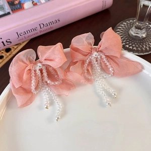 Close-up of pink chiffon bow earrings with crystal beads and long pearl tassels