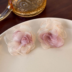Close-up of elegant mesh flower earrings with soft gradient petals on a ceramic dish