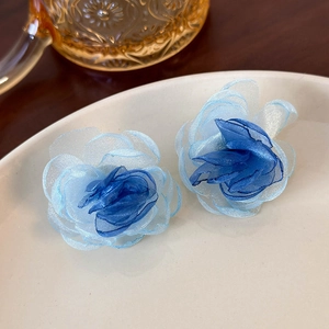 Detailed close-up of blue organza flower earrings on a white ceramic plate