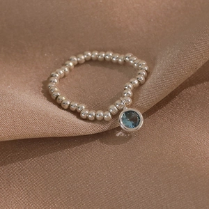 Détail de la bague en perles argentées avec pendentif pierre bleue sur soie couleur champagne