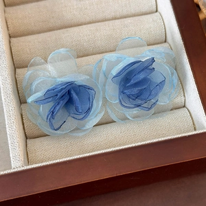 Detailed close-up of blue mesh flower earrings with layered fabric texture in a wooden box
