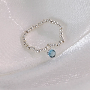 Gros plan d'une bague en argent perlé avec un pendentif rond en zircon bleu clair