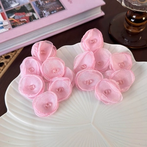 Macro detail of pink fabric flower earrings with crystal beads on a white shell plate