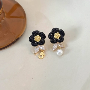 Detailed macro view of black enamel camellia earrings with pearl and zircon charms