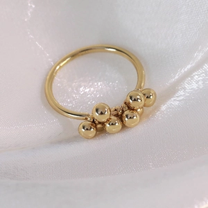 Macro detail of a polished gold minimalist ring with small metal beads on white silk