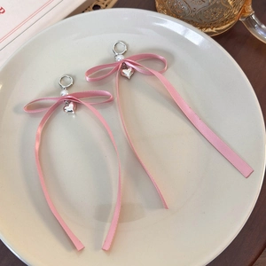 Dettaglio ravvicinato di orecchini a fiocco rosa con ciondolo a cuore e perla elegante