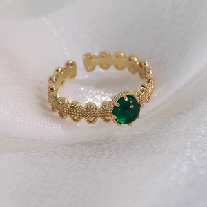Détail macro d'une bague vintage plaquée or avec pierre verte ronde et anneau en dentelle