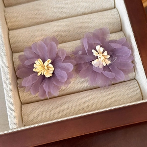 Macro detail of purple mesh flower earrings with layered petals in a wooden jewelry box