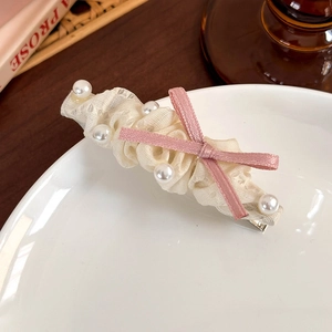 Détail d'une pince à cheveux en dentelle crème avec perles et nœud rose sur assiette
